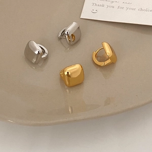 Polished gold and silver geometric square earrings in a beige ceramic dish