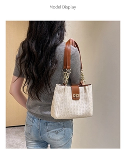 Model wearing straw shoulder bag with brown leather trim and golden chain strap