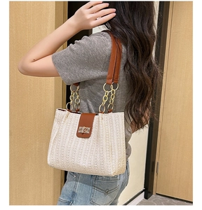 Detail of beige straw tote bag with brown leather strap and gold chain accent