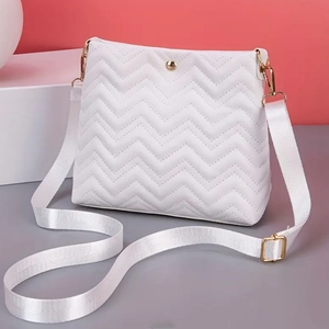Detail of white quilted crossbody bag with wave patterns and golden hardware