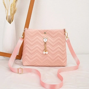Detail of pink quilted crossbody bag featuring gold cat charm and pearl pendants