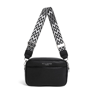 Borsa a tracolla minimalista in pelle nera con ampia tracolla geometrica su sfondo bianco