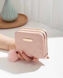 Close-up of pink quilted double zipper wallet with gold metal logo and pompom charm