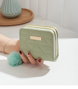 Detail of light green quilted faux leather wallet with double zipper and plush pom-pom charm