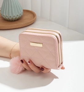 Detailed view of pink quilted double zipper wallet with pompom and metal plaque