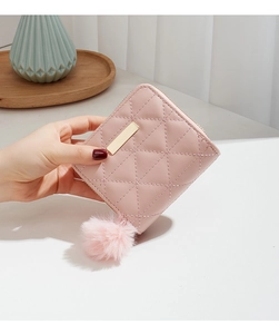 Macro detail of pink quilted faux leather wallet featuring a gold metal bar and pompom charm