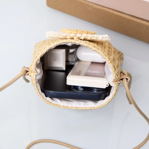 Mini straw woven crossbody bag with white flower charm showing interior storage for phone
