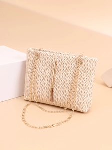 Close-up of beige woven envelope bag with gold tassel charm and chain strap detail