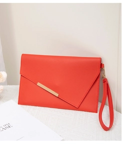 Detail of orange envelope clutch bag with golden metal trim and leather wrist strap