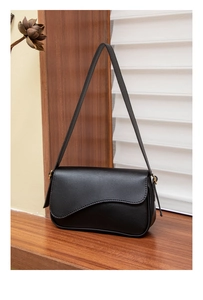 Detail of black pebbled leather shoulder bag with irregular flap and gold hardware accents