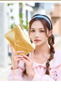 Outdoor shot of a gold envelope clutch with crocodile embossing and a fine chain strap