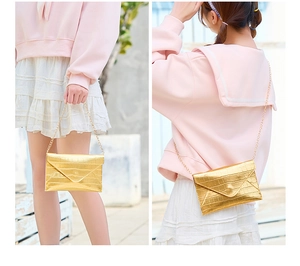 Detail of gold crocodile embossed clutch bag with sleek metal chain and envelope flap
