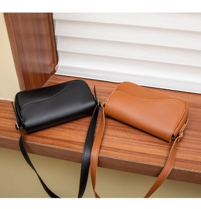Close-up of black and brown faux leather crossbody bags with gold hardware on wood