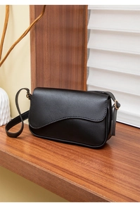 Detail of black crossbody bag with unique wavy asymmetrical flap and gold hardware