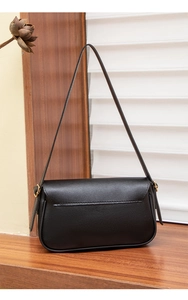 Detailed close-up of a black minimalist leather baguette bag on a rustic wooden ledge