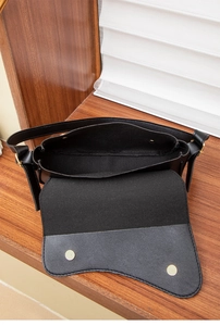 Detail of black leather saddle bag interior showing gold magnetic snap closures and main compartment