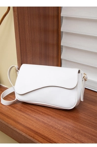 Detail of white cross-body bag featuring asymmetrical flap and gold-tone hardware
