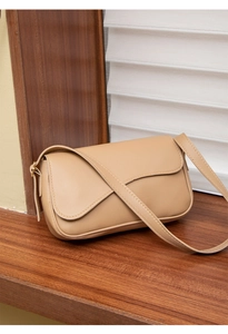 Close-up of beige leather crossbody bag with lychee texture on dark wood stand