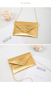 Macro detail of gold envelope bag with crocodile texture and golden chain strap