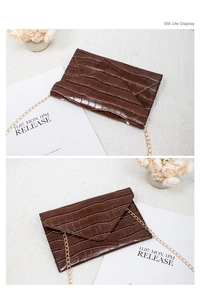 Detail of dark brown croc-embossed envelope clutch with elegant gold chain strap