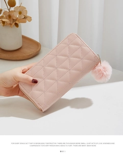 Pink quilted long wallet with zipper and pompom charm held in hand against home decor