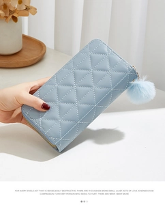 Detail of light blue quilted long wallet with soft pompom charm and zip closure