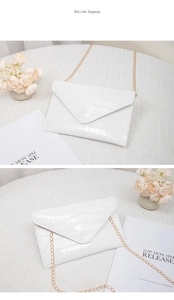 Detail of white crocodile embossed envelope clutch bag with fine gold chain strap