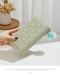 Detail of mint green quilted long wallet with double zipper and fuzzy pom-pom charm