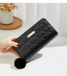 Detail of black quilted long wallet with golden zipper and plush ball pendant
