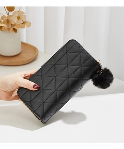 Close-up of black quilted long wallet with golden zipper and black pompom charm