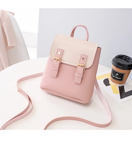 Detail of a pink and cream mini backpack featuring golden buckles on a white table