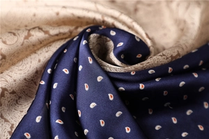 Detailed close-up of dark blue and beige paisley silk scarf with soft drape and glossy finish