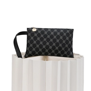 Minimalist black printed clutch bag with gold zipper on white tiered paper platform