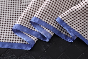Detail of houndstooth silk scarf showing brown pattern with blue hem on leather surface