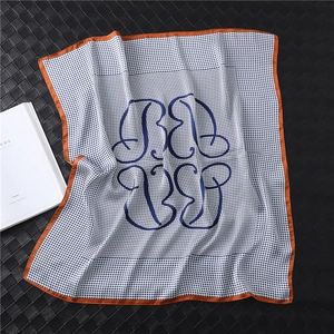 Detailed view of silk-like blue houndstooth square scarf with orange borders and B-letter