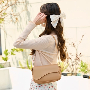 Light brown leather shoulder bag with wave curved flap shown in a stylish outdoor setting