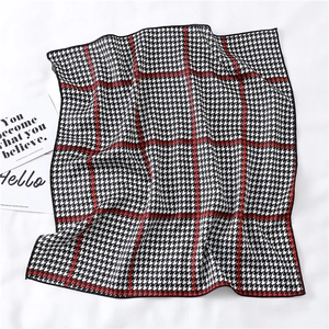 Close-up of red plaid houndstooth silk scarf on white fabric with decorative cards