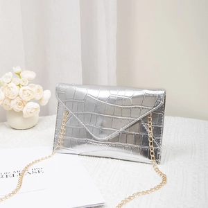 Silver crocodile texture envelope clutch bag with gold chain strap on white table