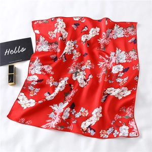 Detail of red silk scarf with floral and butterfly prints laid on a white fabric