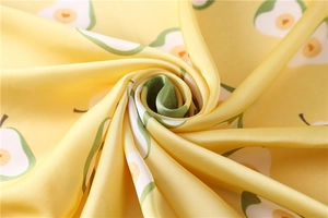 Dettaglio macro di un foulard in seta con stampe realistiche di avocado su tessuto giallo