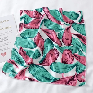 Detailed close-up of white silk scarf with pink and green feather print and fine stitching