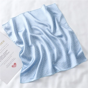 Detail shot of light blue polka dot silk scarf with elegant wedding card on white fabric