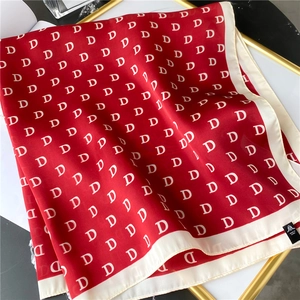 Detail shot of a red silk scarf featuring white letter D monogram prints and stitched edges