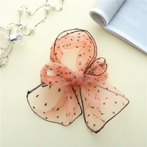 Détail d'un foulard en crépon rose à pois verts posé sur une table élégante