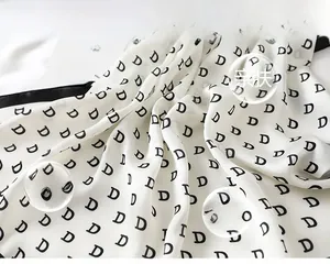 Detailed view of white satin scarf featuring repeating black letter D pattern and smooth texture