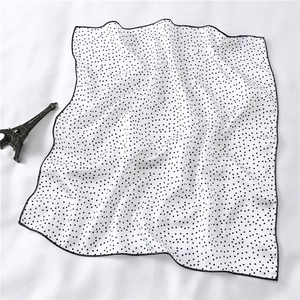 Close-up of white silk square scarf with black polka dots and fine black hem edges