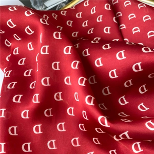 Close-up of red silk scarf fabric with white letter D monogram pattern and smooth texture