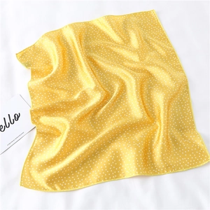 Detailed close-up of yellow silk scarf with white polka dots and satin texture