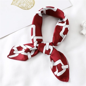 Detail of red and white chain print silk scarf tied in a knot on a white background