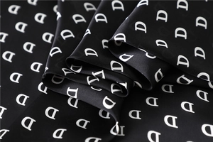 Macro detail of silk-like black fabric with white D letter pattern and soft luster